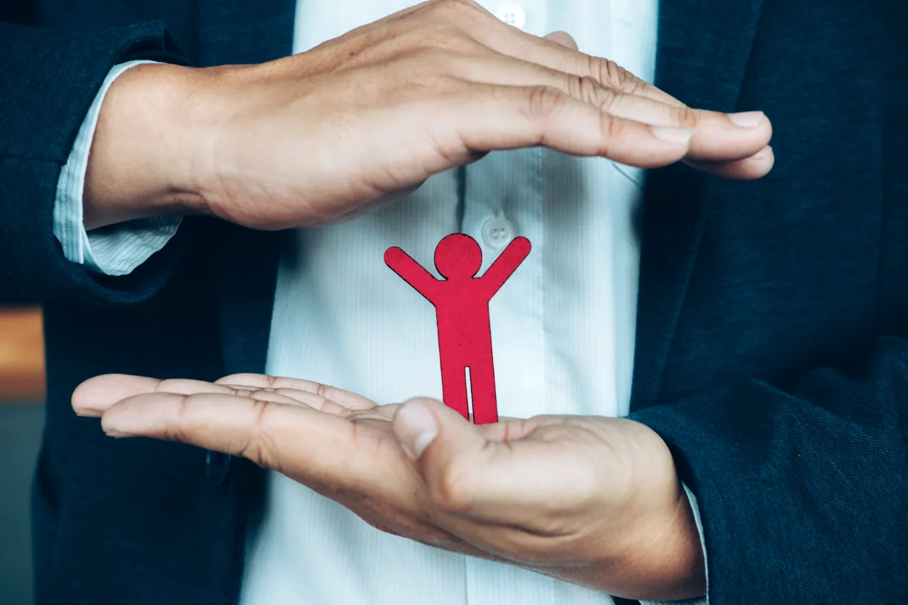 Welfare aziendale e tutela dei dipendenti Mani di un professionista che proteggono una sagoma stilizzata che rappresenta la tutela e il benessere del dipendente tramite welfare aziendale